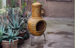 Rode Sol-y-Yo Chimenea Mexicaanse vuurpot van 105 cm hoog, terracotta ontwerp met zondecoratie, geplaatst in een sfeervolle tuinomgeving.
