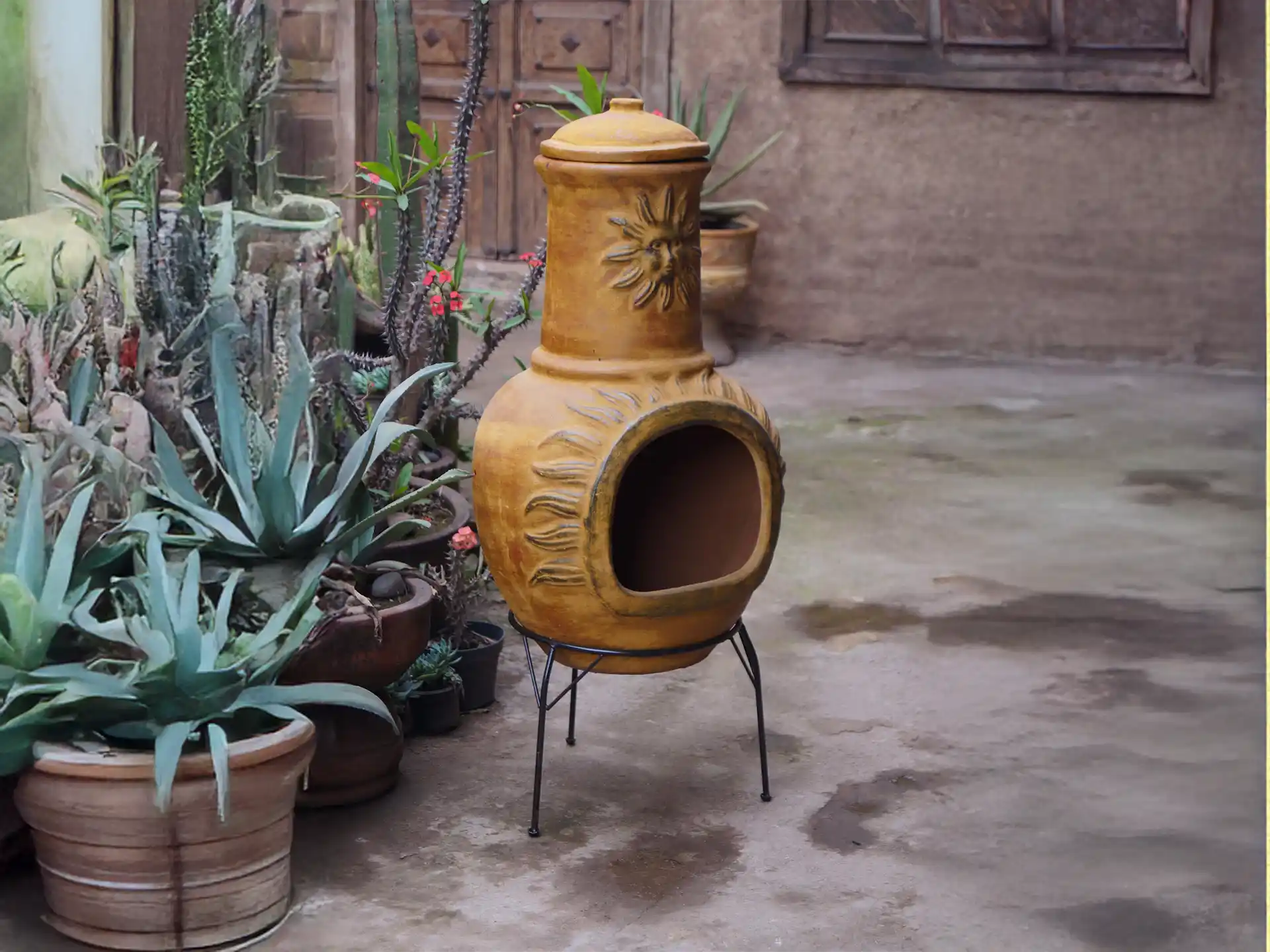 Rode Sol-y-Yo Chimenea Mexicaanse vuurpot van 105 cm hoog, terracotta ontwerp met zondecoratie, geplaatst in een sfeervolle tuinomgeving.