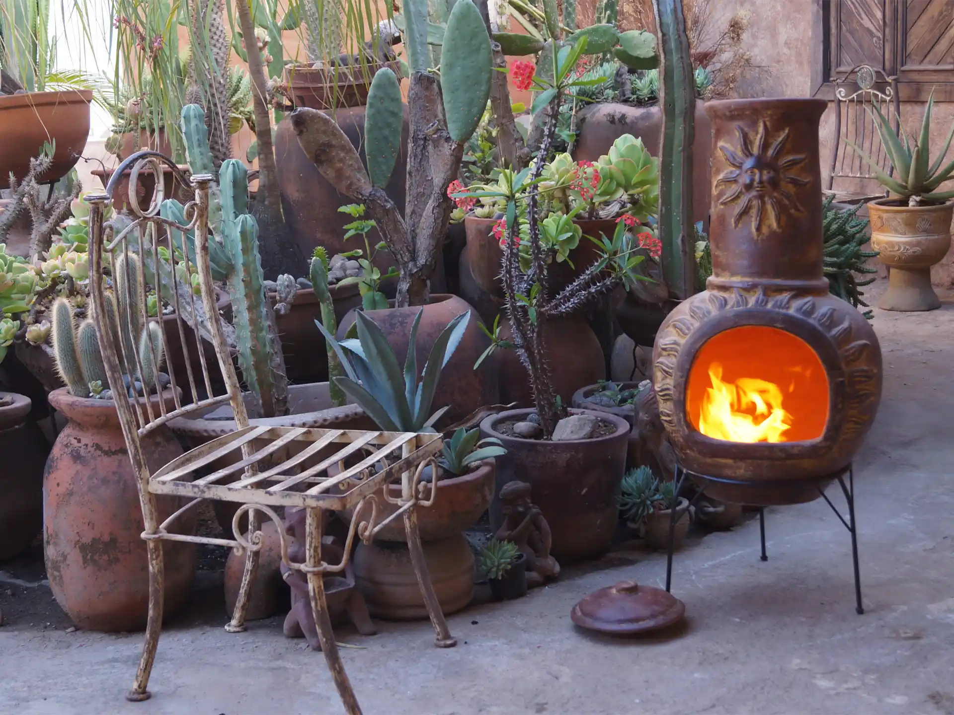 Sfeerfoto van de rode Sol-y-Yo Chimenea Mexicaanse vuurpot met zonmotief (105 cm), brandend met houtvuur in een tuin voor warmte en gezellige sfeer.