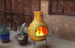 Sfeerfoto van de gele Sol-y-Yo Jumbo XL brede terrashaard (115 cm) met zondecoratie, inclusief voet en deksel, sfeervol brandend met open vuur in een tuinomgeving voor warmte en gezelligheid.