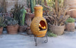Sfeerfoto van de gele Sol-y-Yo Mexicaanse Chimenea tuinhaard Madrid met zon (46 x 106 cm), brandend met open vuur in een sfeervolle tuinomgeving voor warmte en gezelligheid.