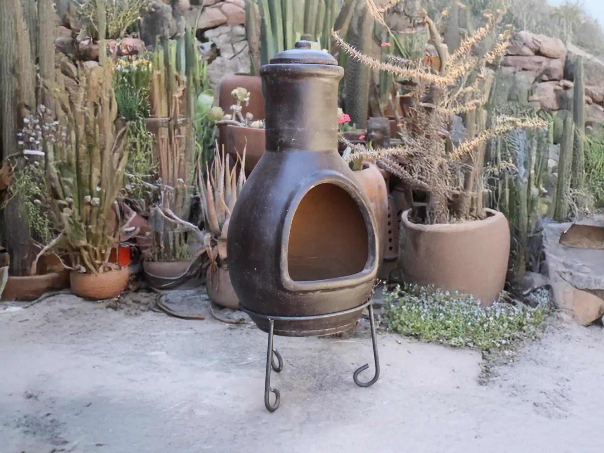 Sfeerfoto van de grijze Sol-y-Yo Mexicaanse tuinhaard (46 x 106 cm), brandend met open vuur in een sfeervolle tuinomgeving voor warmte en gezelligheid.