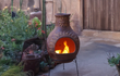 Sfeerfoto van de rode Sol-y-Yo XL Chimenea Mexicaanse terrashaard Jumbo (115 cm) met zondecoratie, sfeervol brandend met open vuur in een tuinomgeving voor warmte en gezelligheid.