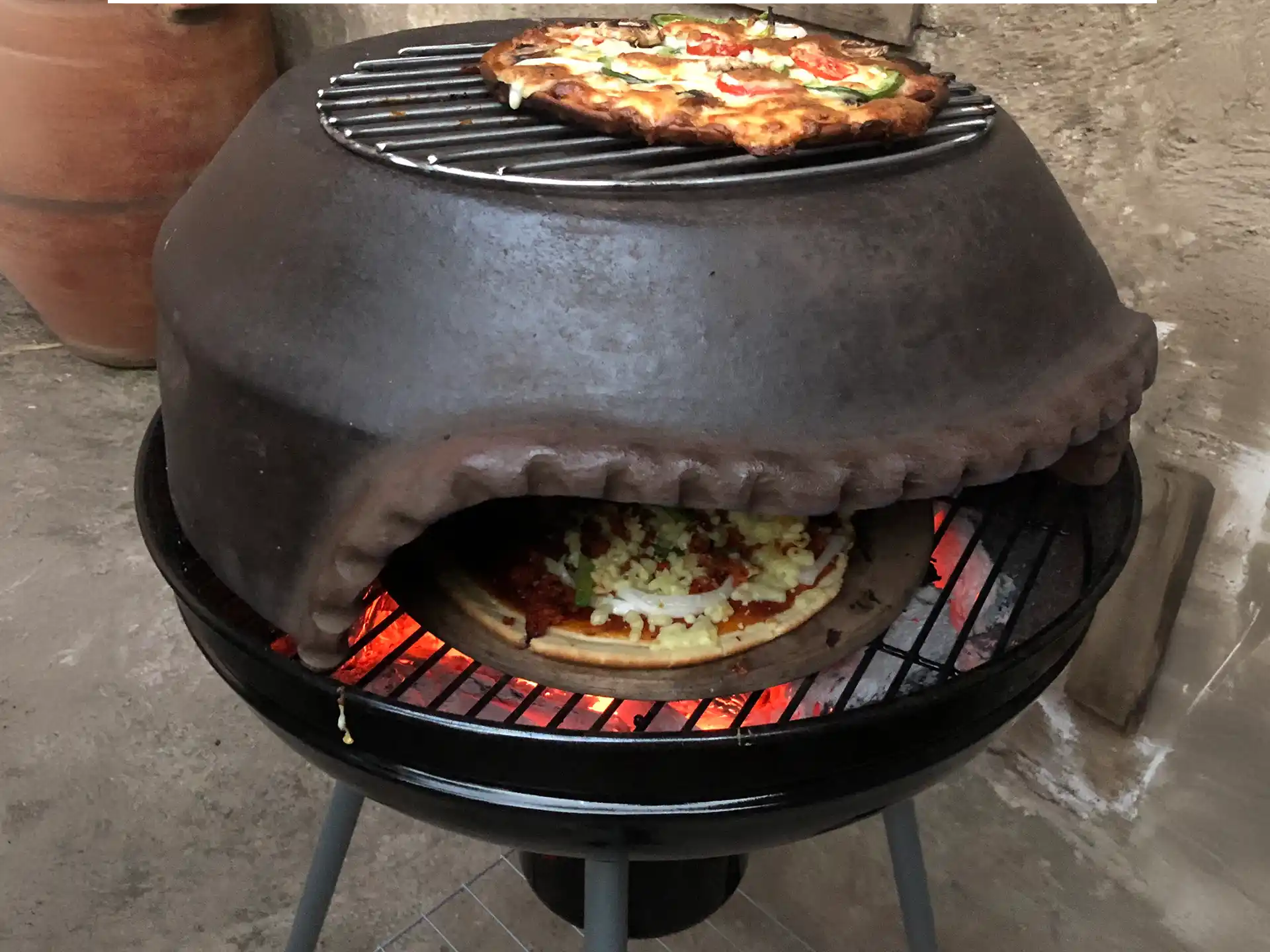 Sol-y-Yo Pizza Dome stenen koepeloven ø54 cm, in gebruik op barbecue, pizza wordt gebakken boven houtskoolvuur.
