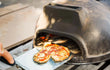 Sol-y-Yo Toscaanse stenen pizza oven 52 cm, houtgestookt, pizza schuift in oven via metalen schep, buiten in gebruik.