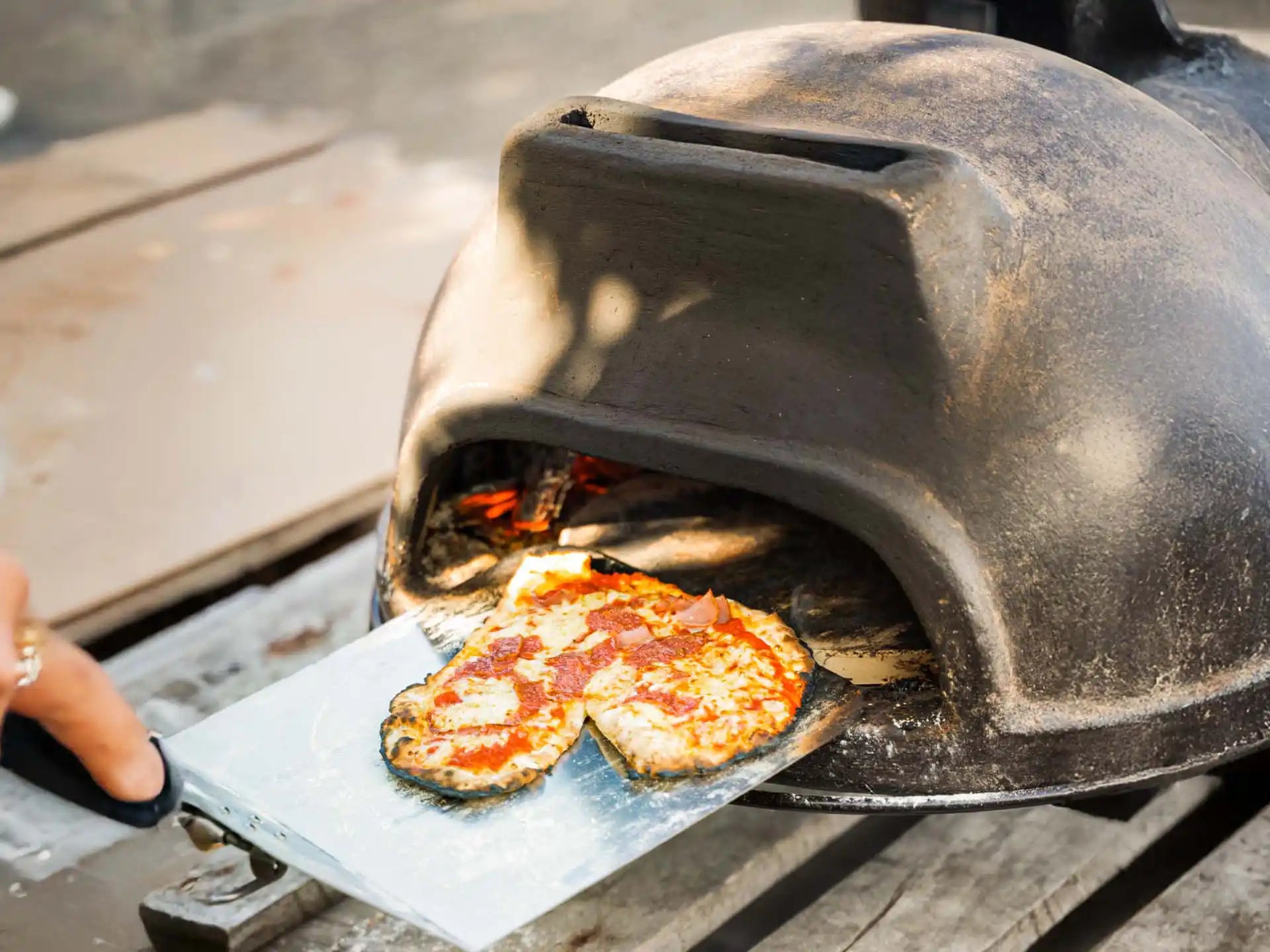 Sol-y-Yo Toscaanse stenen pizza oven 52 cm, houtgestookt, pizza schuift in oven via metalen schep, buiten in gebruik.