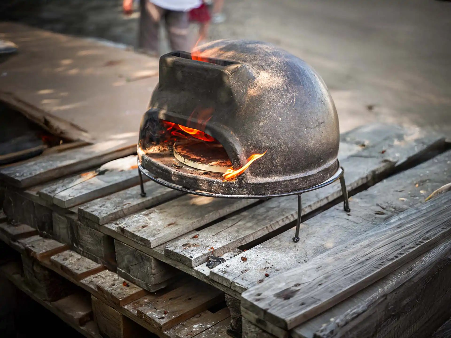 Sol-y-Yo Toscaanse houtgestookte pizza oven 52 cm, geplaatst buiten op houten vlonder, oven in gebruik met vlammen.