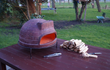 Sol-y-Yo Venetiaanse houtgestookte pizza oven 52 cm, buiten geplaatst op houten tafel, klaar voor gebruik met houtblokken ernaast.