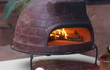 Sol-y-Yo Venetiaanse stenen pizza oven 52 cm, houtgestookt model op metalen onderstel, in gebruik met brandend vuur in de oven.