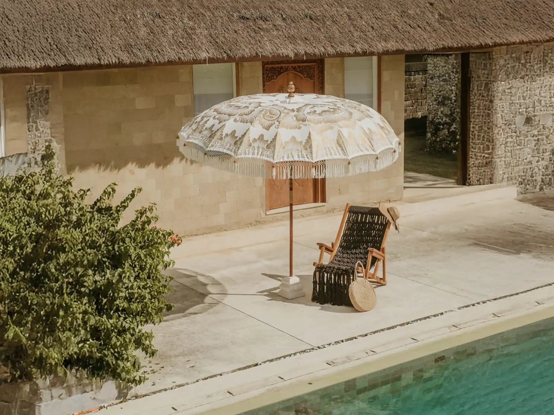 Balinese parasol in crème met volledig gouden schildering en franjes naast een zwembad, ideaal voor een tropische loungesfeer.