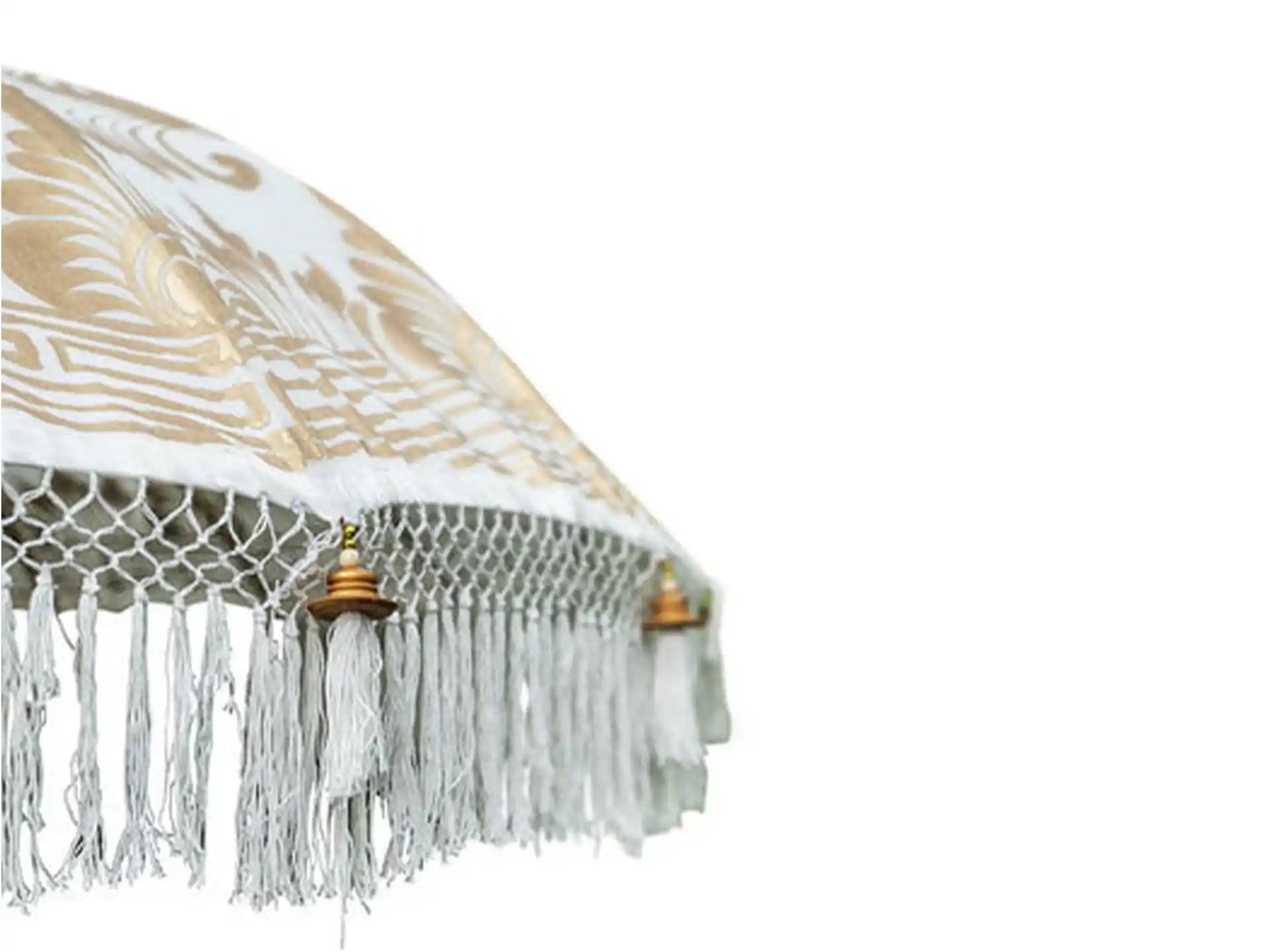 Close-up van een Balinese parasol in crème met volledig gouden handbeschildering en decoratieve franjes, luxe uitstraling voor tuin en terras.