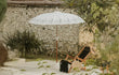 Balinese parasol in crème met half zilveren beschildering in een tuinsetting naast een houten ligstoel, perfect voor schaduw en stijl.