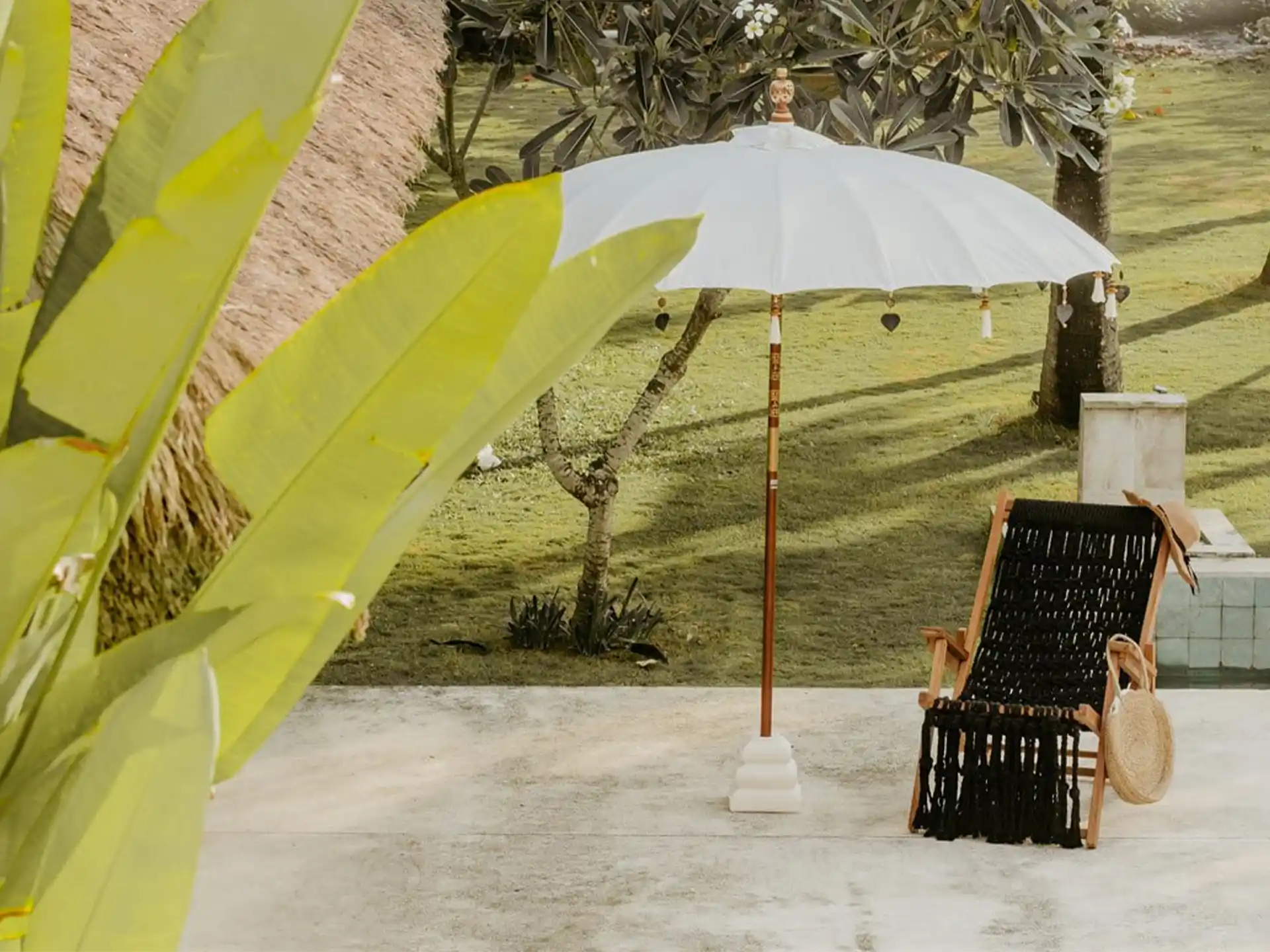 Todo Bien Bali parasol in crème kleur geplaatst in een tuin naast een houten ligstoel, ideaal voor een zomerse en sfeervolle buitenruimte.