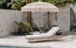 Stijlvolle crème Bali parasol met macramé details en franjes, geplaatst naast een modern zwembad met tropische planten en loungebed, perfect voor een bohemian tuinsetting.