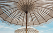 Detailopname van een crème Bali parasol met macramé franjes, gezien van onderaf tegen een heldere blauwe lucht, sfeervol bohemian design voor tuin of terras.