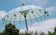 Lichtblauwe Todo Bien Bali parasol geplaatst in een tropische tuin met palmbomen, perfect als stijlvolle en handgemaakte schaduwbrenger.