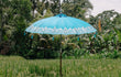Bali parasol in helder zeeblauw met zilveren handbeschildering, geplaatst in een rijstveld omringd door tropische vegetatie.