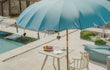 Sfeerfoto van de Todo Bien Bali parasol zeeblauw bij een zwembad, met houten tafel, fruit en stoel voor een zomerse luxe uitstraling.