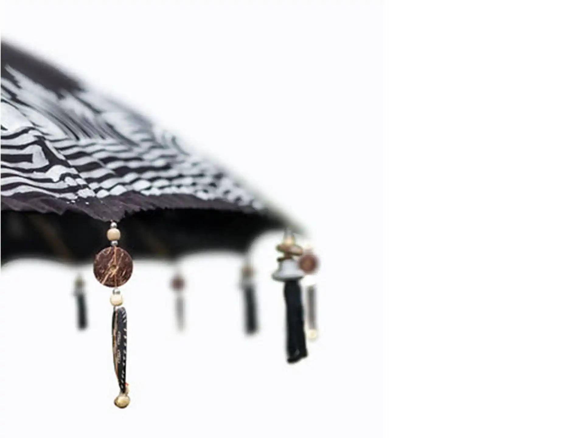 Close-up van de rand van de Todo Bien Bali parasol in zwart met handgeschilderde zilveren details en decoratieve hangers.