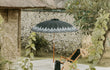 Sfeervolle opstelling van de zwarte Bali parasol met zilveren beschildering bij een ligstoel naast een stenen muur.